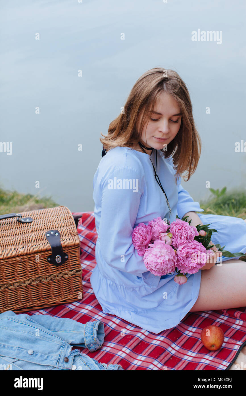 Frau mit Blumen sitzen auf der Picknickdecke am Fluss Stockfoto
