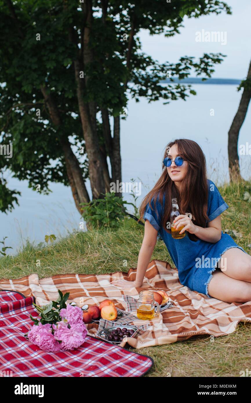 Frau sitzt auf der Picknickdecke mit einem Getränk Stockfoto