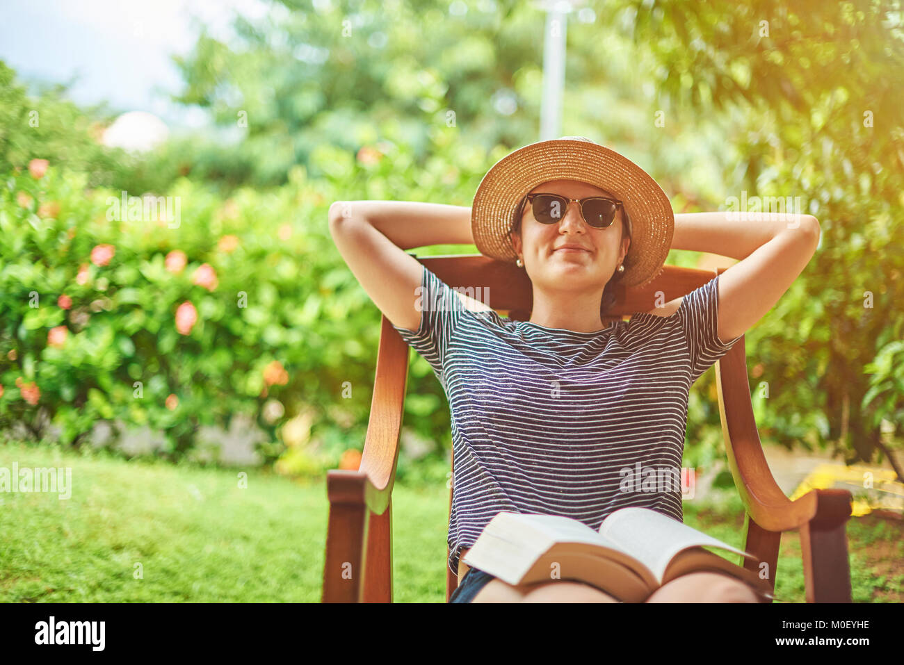 Junge Frau mit Buch auf den Knien am sonnigen Sommer Stockfoto