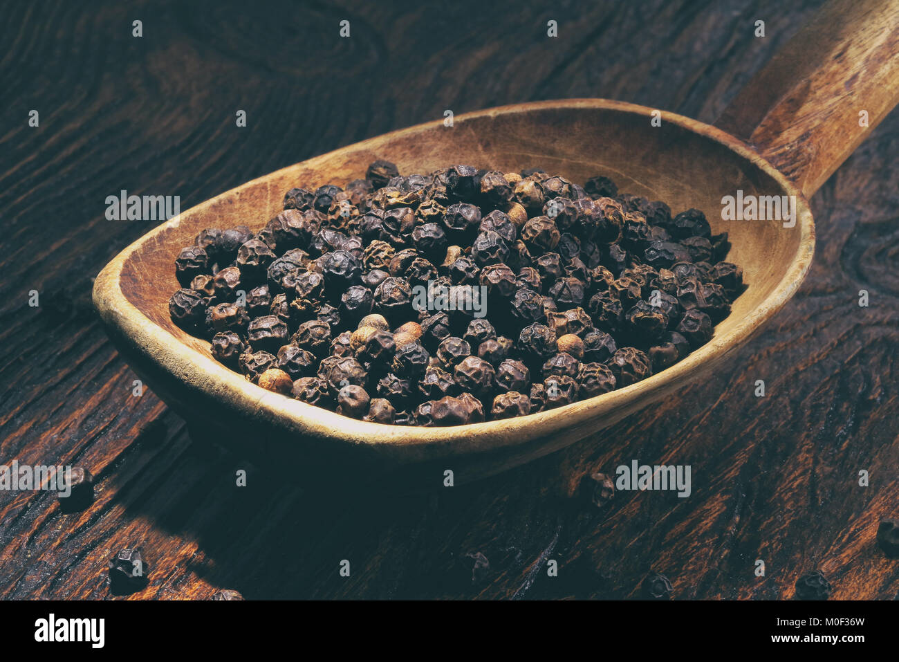 Schwarzer Pfeffer in Löffel aus Holz auf Holz- Tabelle Stockfoto