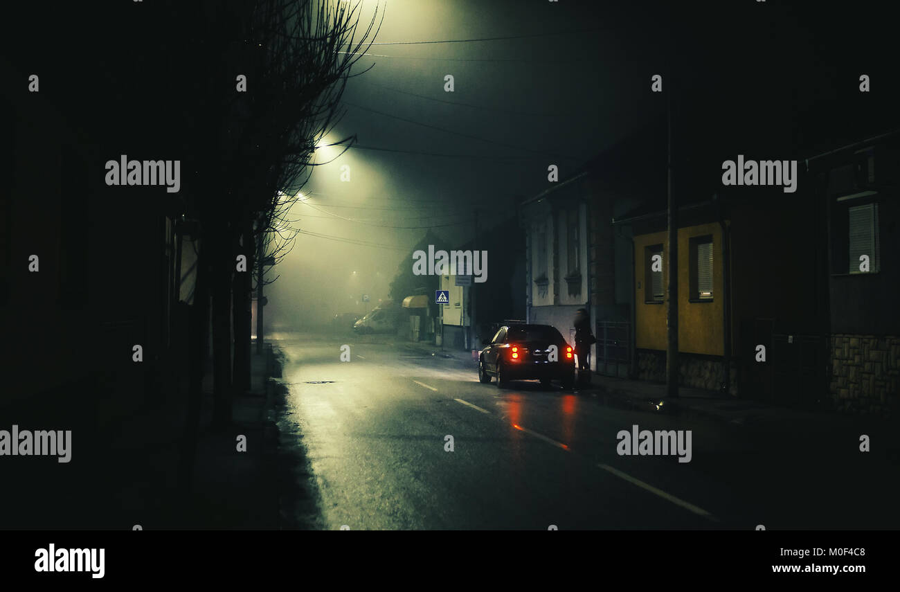 Nacht Szene auf nebligen Straße, einer kleinen Stadt, einsame Frau und ein Auto. Stockfoto