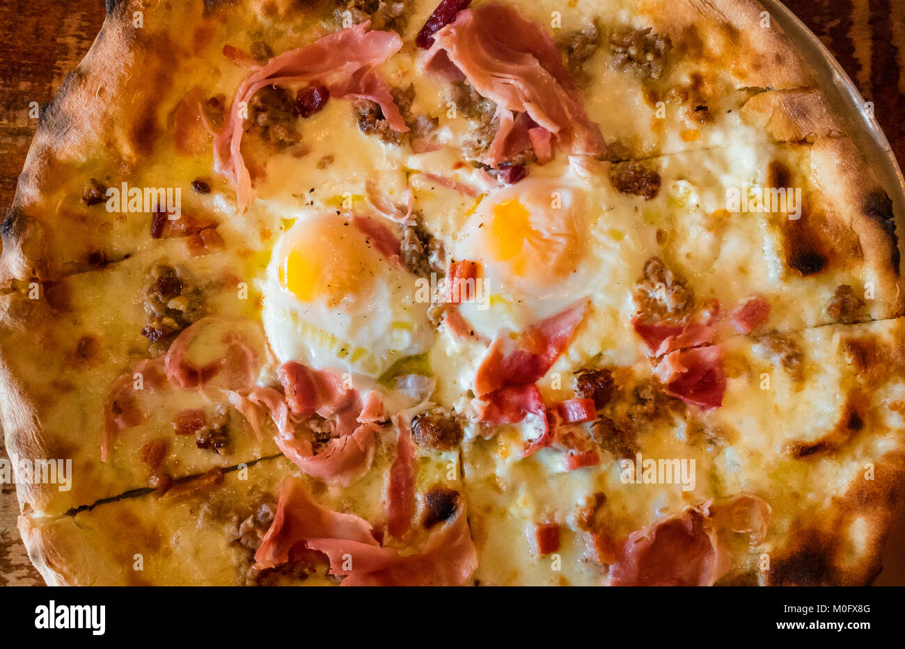 Eine Frühstückspizza mit Mozzarella-Käse, gekochtem Schinken, Wurst und zwei Spiegeleiern, sunnyside up Stockfoto