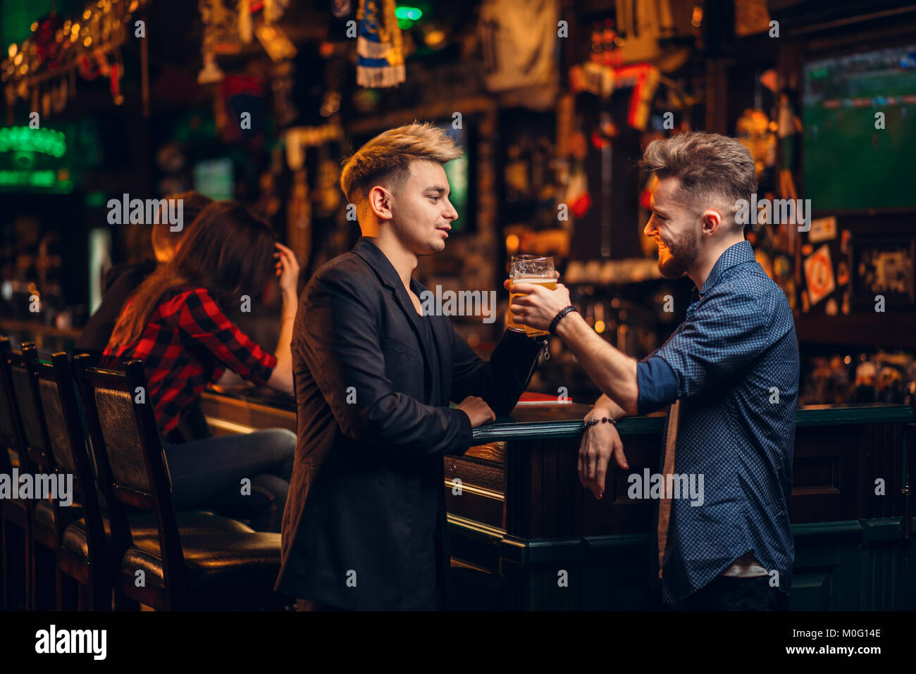 Zwei Männer an der Theke, hob die Gläser mit Bier für den Sieg in Spiel in einem Sport Pub , Freizeit der Fußball-Fans Stockfoto