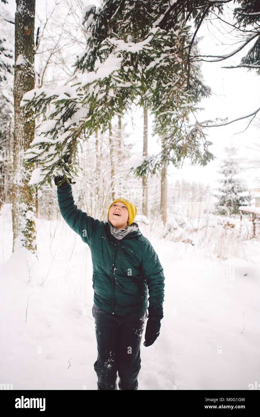 Teenager Boy ist bereit, die Niederlassung zu schütteln und den fallenden Schnee spüren im Winter Wald. Stockfoto