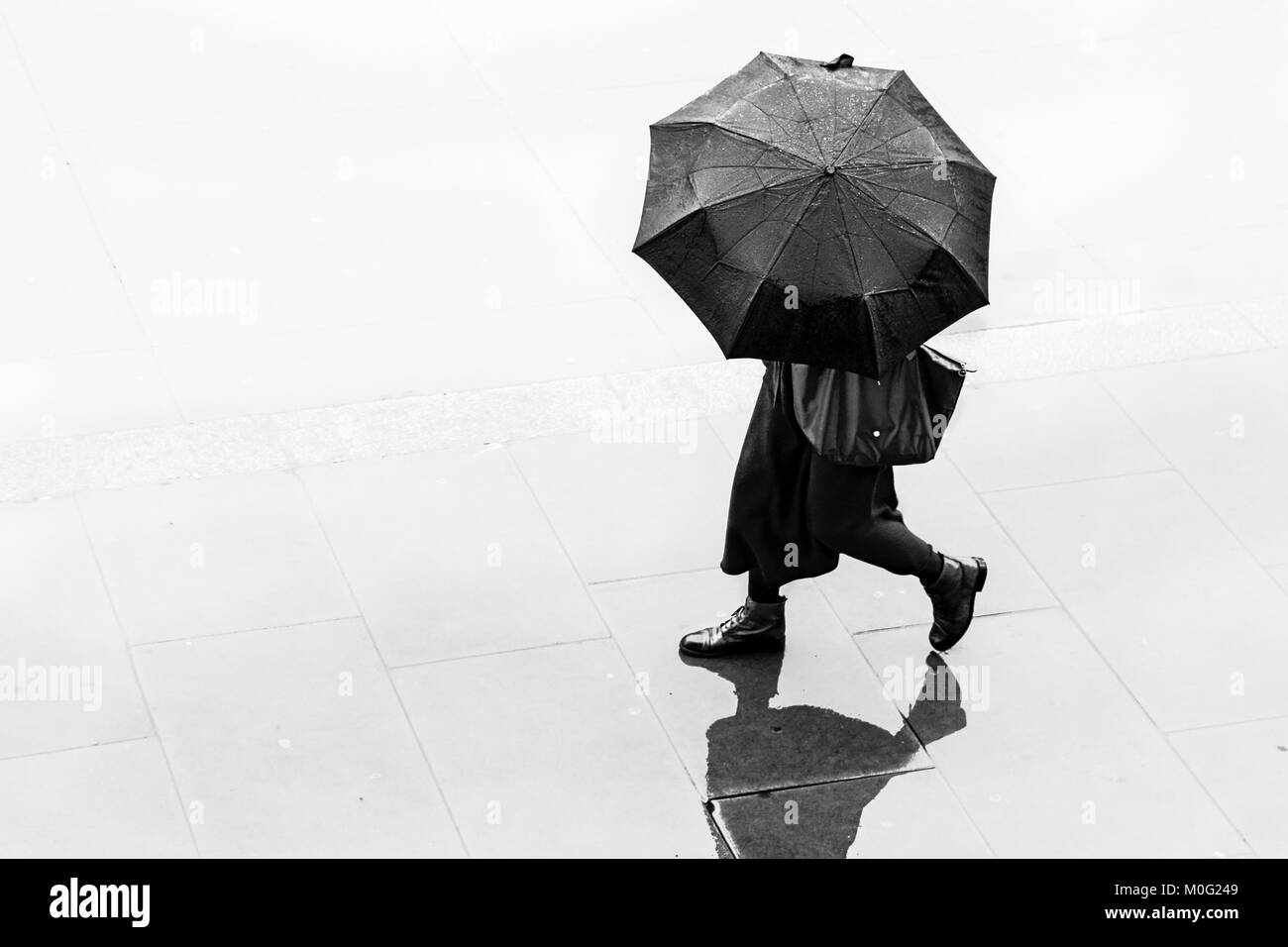 Schwarz-weiß Straßenfotografie in London: Frau, die im Regen mit Regenschirm läuft. Stockfoto