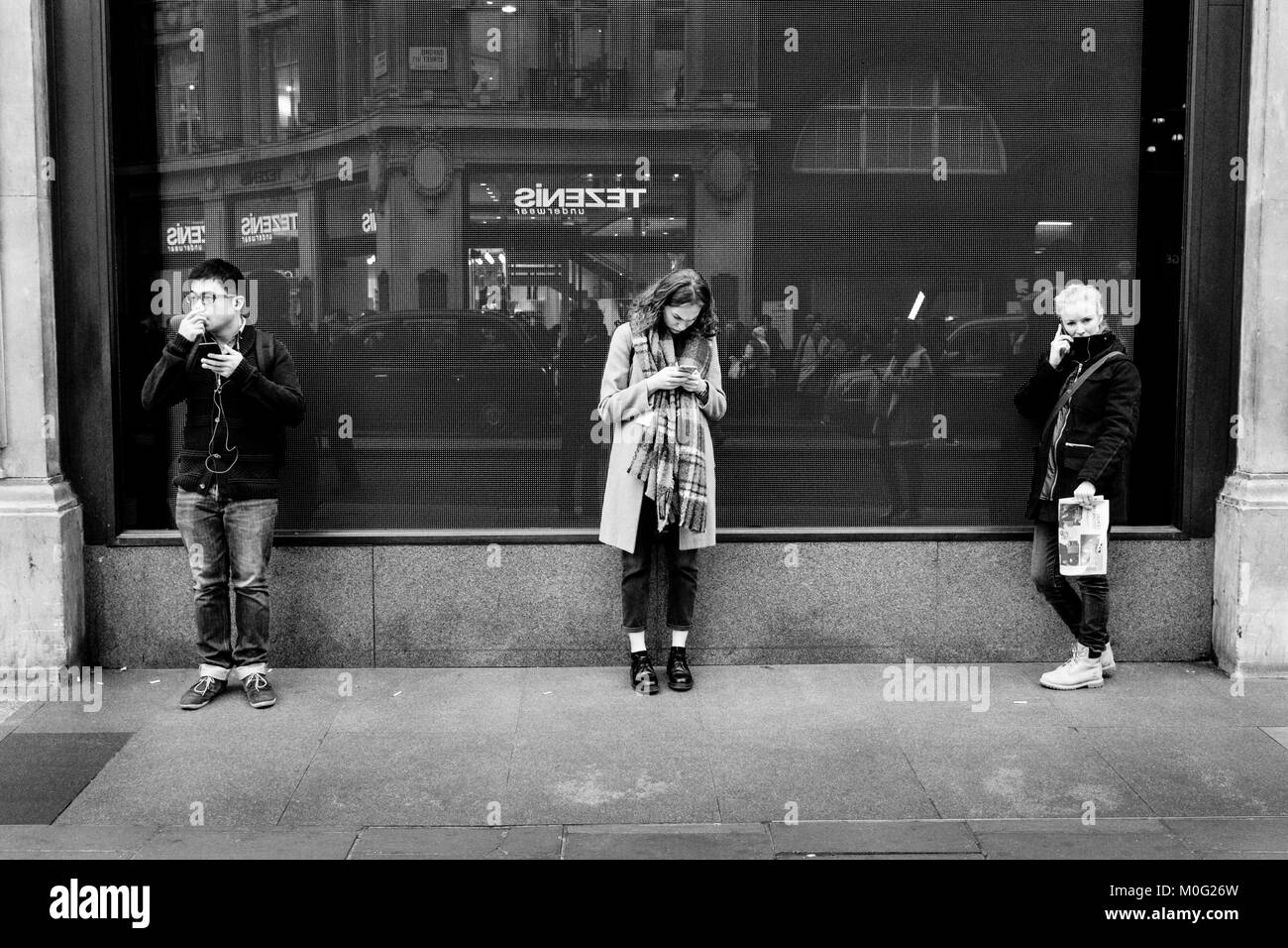 Schwarz-Weiß-Straßenfotografie in London: Drei junge Menschen nutzen Mobiltelefone auf der Straße Stockfoto