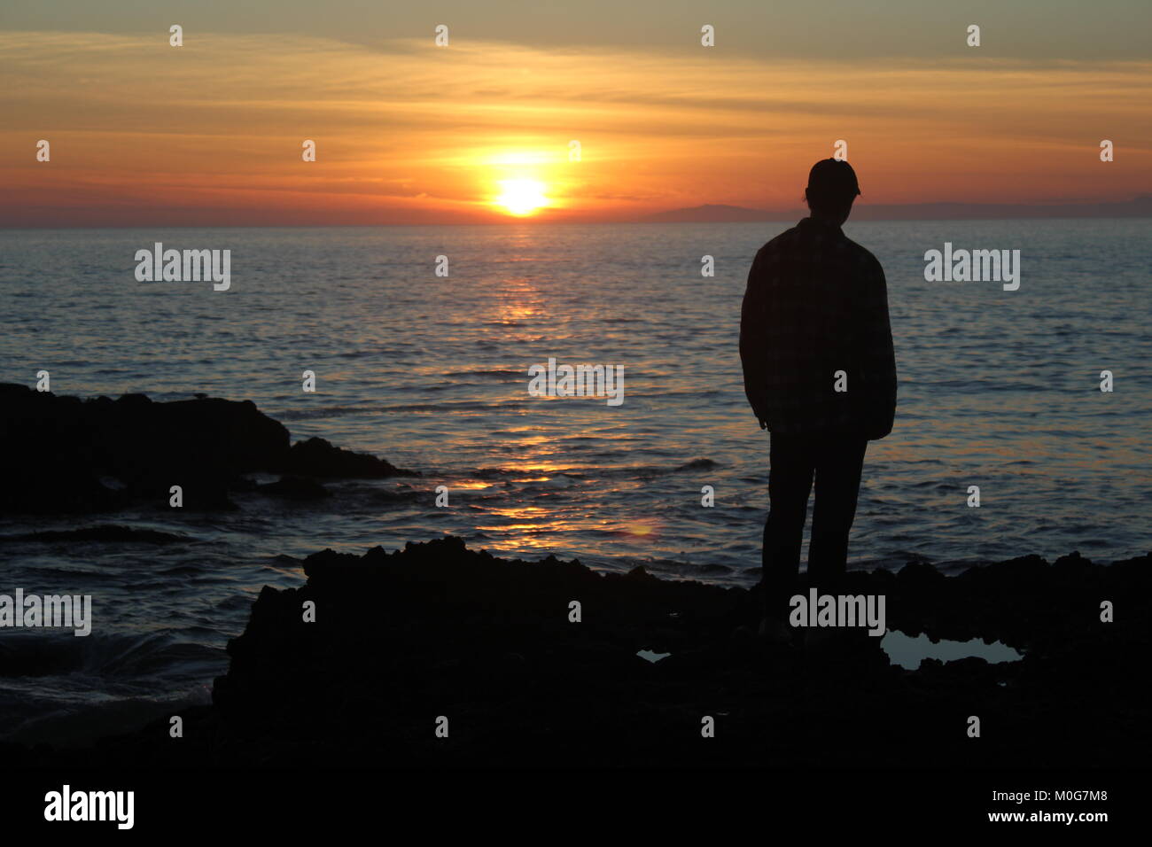 Einen Mann an einem Sonnenuntergang in Laguna Beach. Die Sonne über dem Ozean, als ein junger Mann beobachtet. Stockfoto