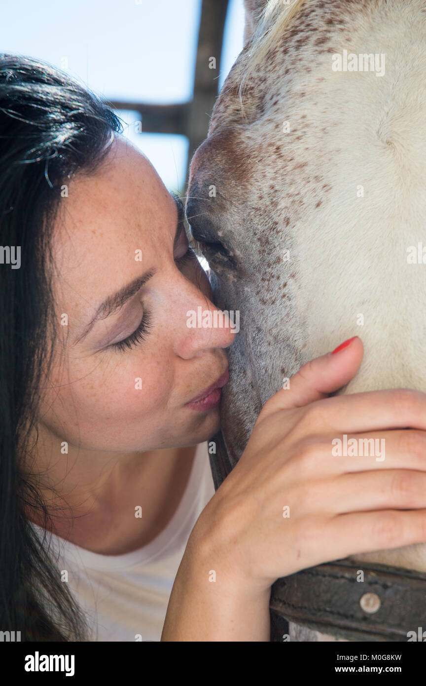 Schwarzhaarige Frauen kuscheln und Küssen ein weißes Pferd in der Backe, in der Nähe Stockfoto