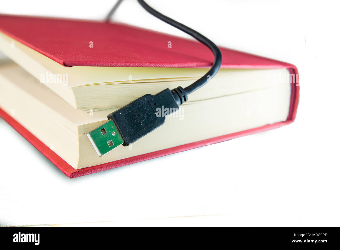 USB-Kabel, das aus einem Buch mit rotem Deckel. Ebook Konzept, Audio Buch Konzept oder Informationstechnologie. Auf weiß isoliert. Stockfoto