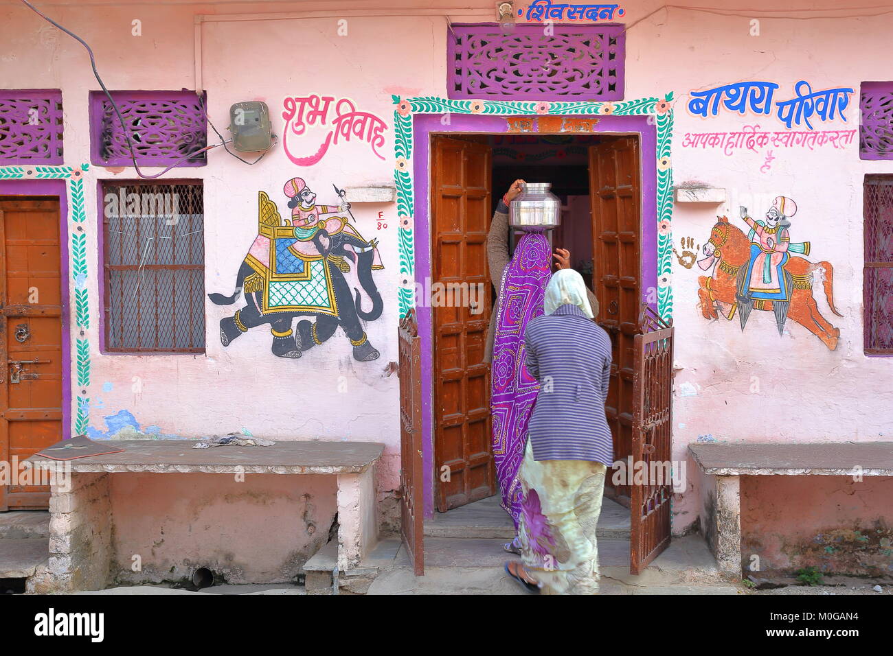 CHITTORGARH, Rajasthan, Indien - Dezember 14, 2017: Eine bunte traditionelles Haus mit Gemälden und eine Frau, die Wasser Topf auf den Kopf Stockfoto