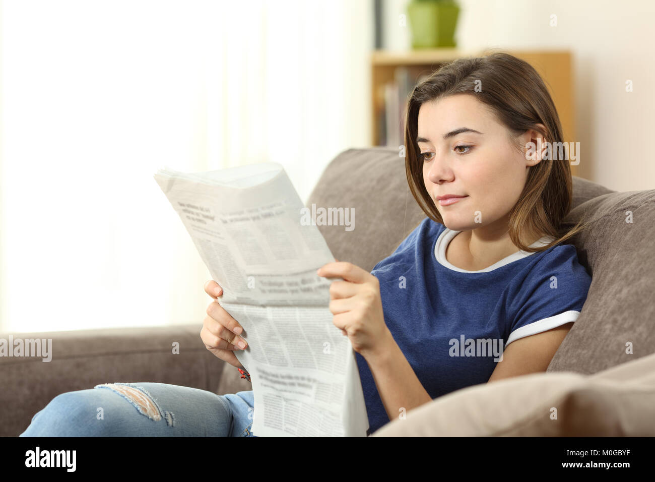 Porträt einer ernsthaften Teenager eine Zeitung lesen auf einer Couch im Wohnzimmer zu Hause sitzen Stockfoto