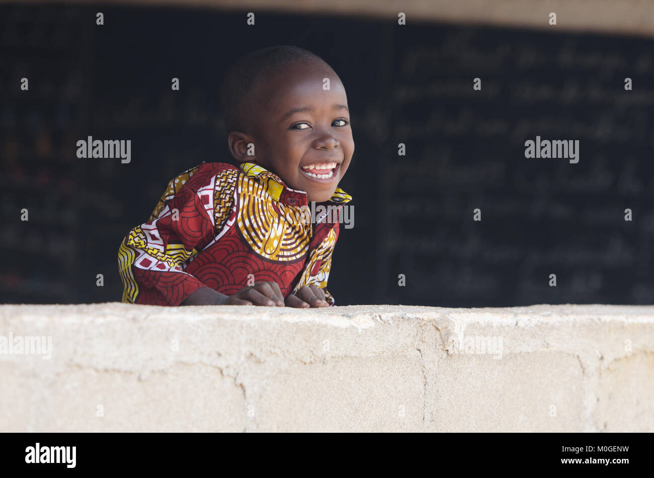 Schöne afrikanische Baby Boy lachend hinter der Wand in der Schule Stockfoto