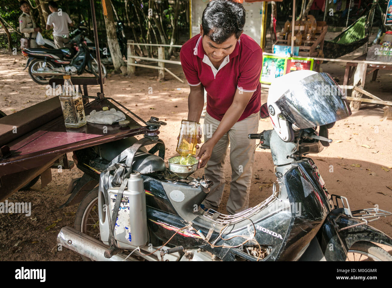 Tuk Tuk Fahrer befüllen Tank mit Kraftstoff aus alten Bourbon Whiskey Flasche, Angkor Thom, Kambodscha. Stockfoto