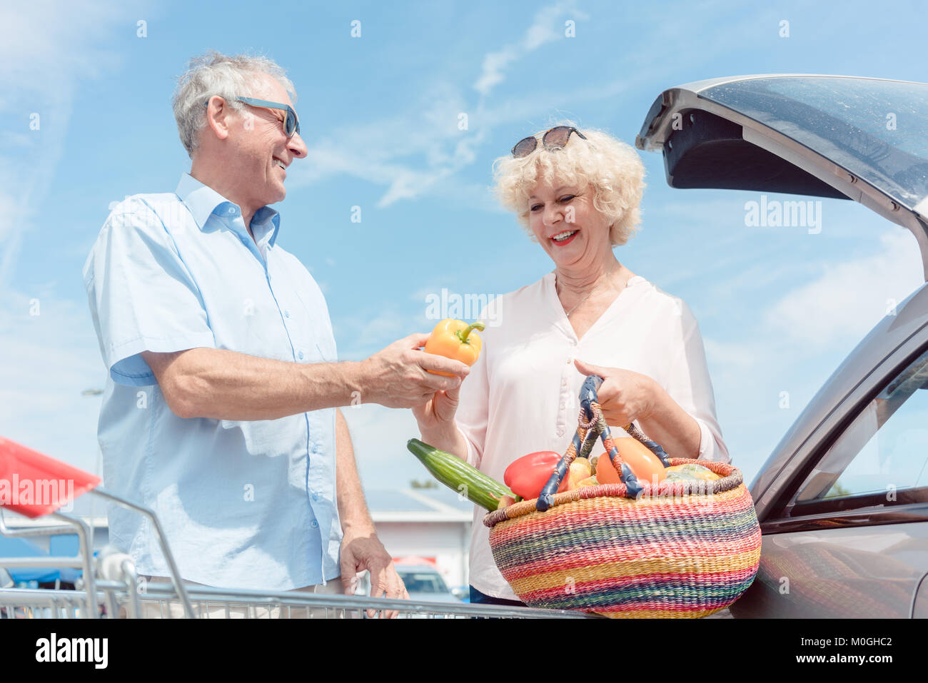 Älterer Mann hält einen Warenkorb, während seine Frau Witz suchen Stockfoto