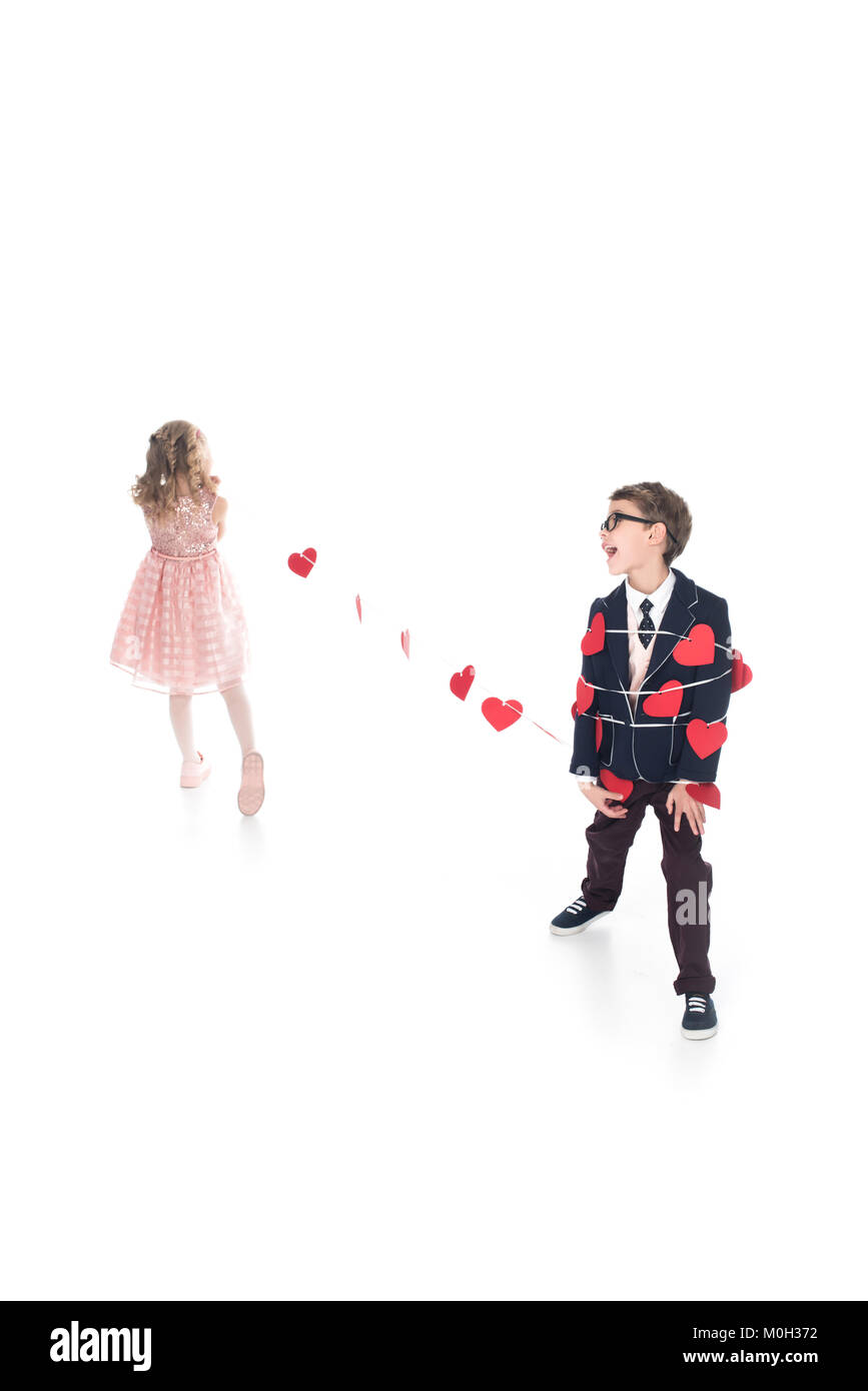Kleines Mädchen binden Stilvolle Junge mit Seil und roten Herzen isoliert auf weißem Stockfoto