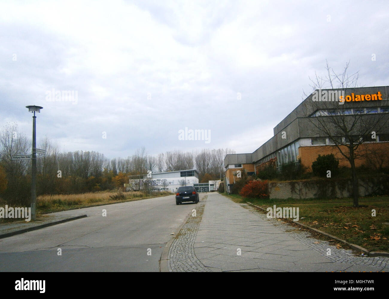 Das Bild mit dem Titel „Buch ErnstBuschstraße W“ zeigt eine Straßenansicht der Ernst-Busch-Straße in Buch, Berlin. Die Szene zeigt Wohngebäude und städtische Infrastruktur, die für die moderne Entwicklung des Viertels charakteristisch sind. Stockfoto