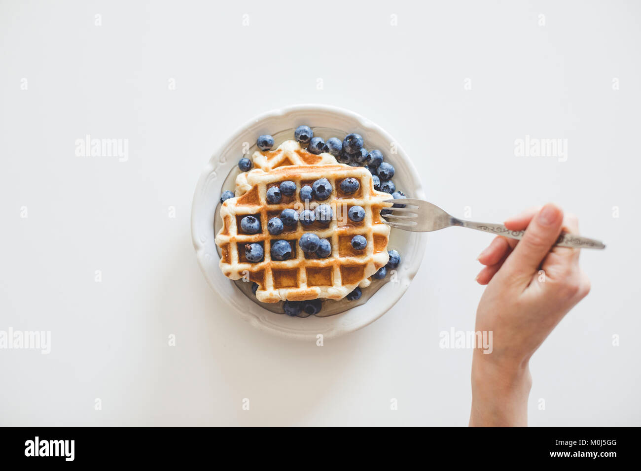 Blick von oben auf die Frau essen Waffeln mit Blaubeeren für Frühstück Stockfoto