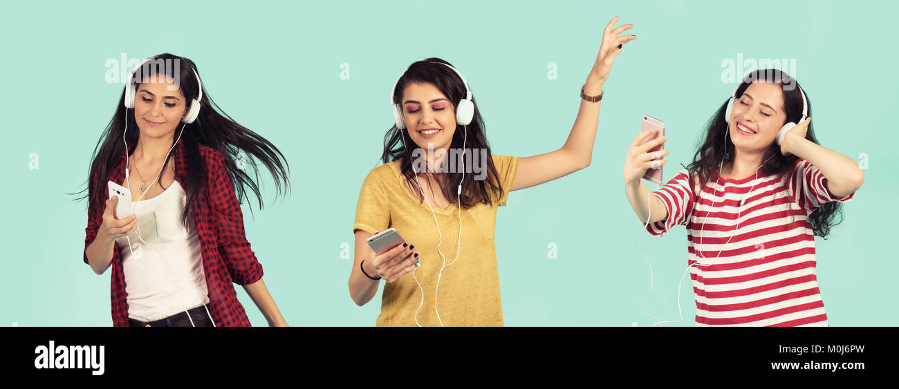 Drei junge Schöne Frauen tanzen und lachen hören die Musik durch die großen Kopfhörer auf ein Smartphone auf grünem Hintergrund verbunden. Stockfoto