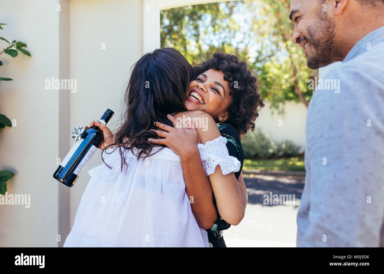 Gruß Frau Paar für ein neues Haus. Lächelnde junge Frau mit Weinflasche gratulieren ihr Freund. Housewarming Party mit Freunden. Stockfoto