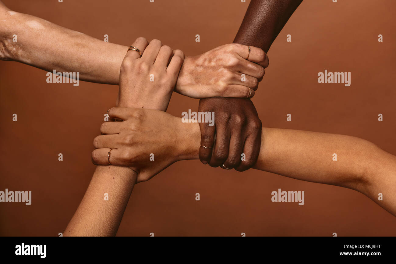 Vier unterschiedlichen Frauen, die sich in jeden anderen Handgelenken in einem Kreis. Blick von oben auf die weibliche Hände in der Sperre gegen braunen Hintergrund verbunden. Stockfoto