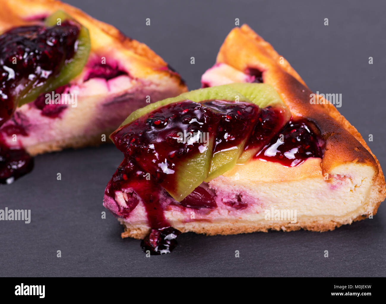 Ein Stück Kuchen aus Quark mit Kirschen mit Marmelade auf einem schwarzen Untergrund gegossen Stockfoto