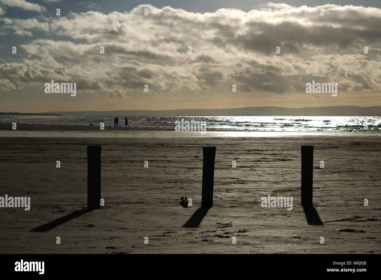 Silhouette von Wellen brechen Beiträge auf Brean Strand mit Menschen gehen der Hund entlang der Küste Stockfoto