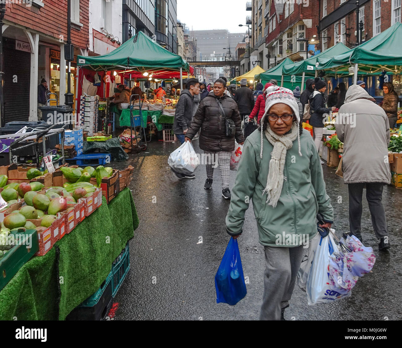 Eine alte Dame Carrier schweren Tragetaschen voller Einkaufen durch Surrey Street Market in Croydon, London. Stockfoto