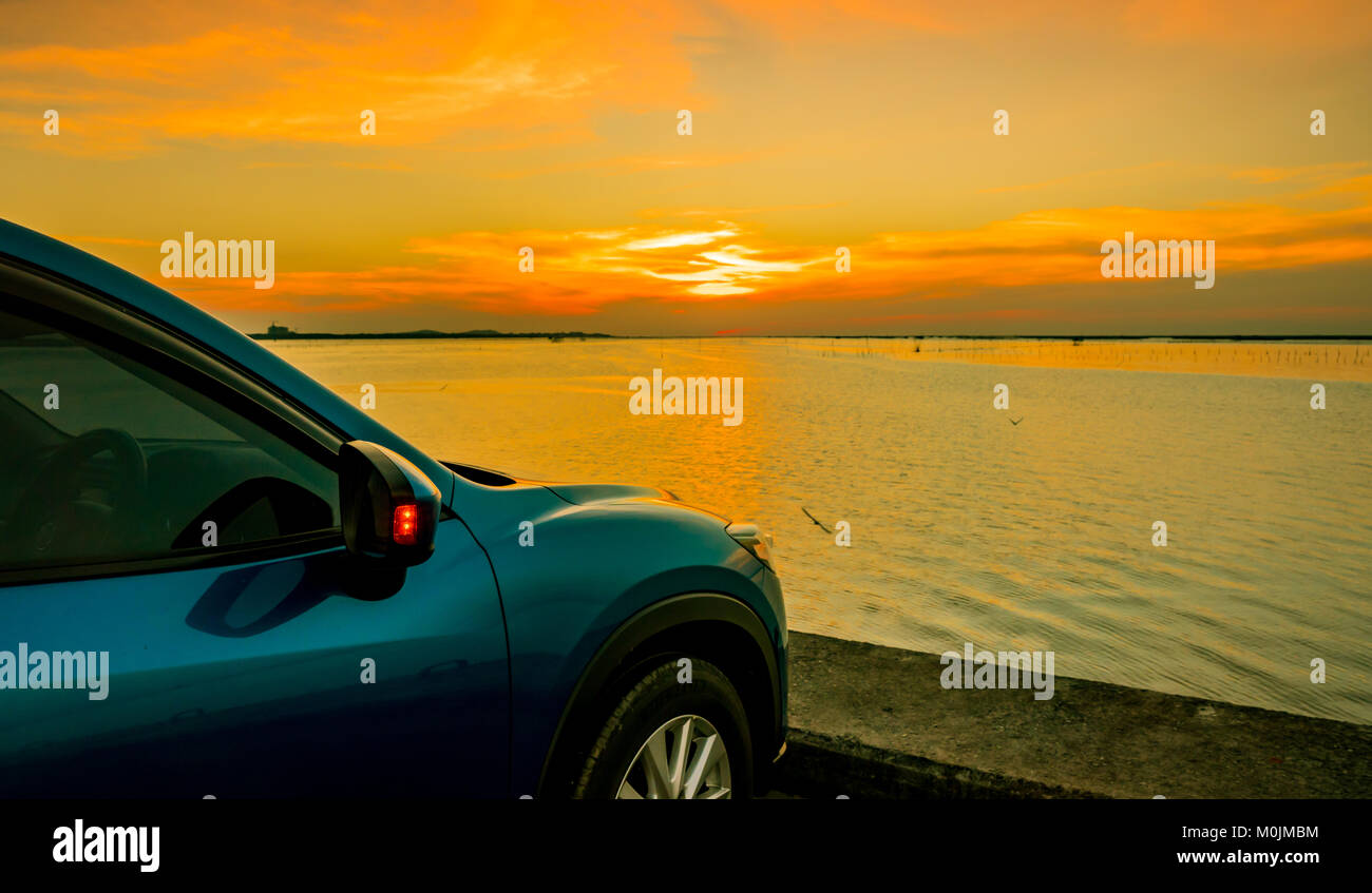 Blaue kompakte SUV-Auto mit Sport und modernes Design auf Beton durch das Meer geparkt bei Sonnenuntergang. Umweltfreundliche Technologie. Geschäftlicher Erfolg Stockfoto