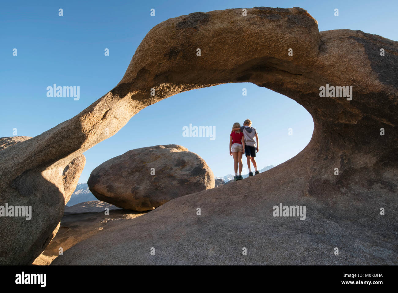 Junge Kinder unter einem natürlichen Felsbogen stehend, Alabama Hills, Kalifornien, Vereinigte Staaten von Amerika Stockfoto