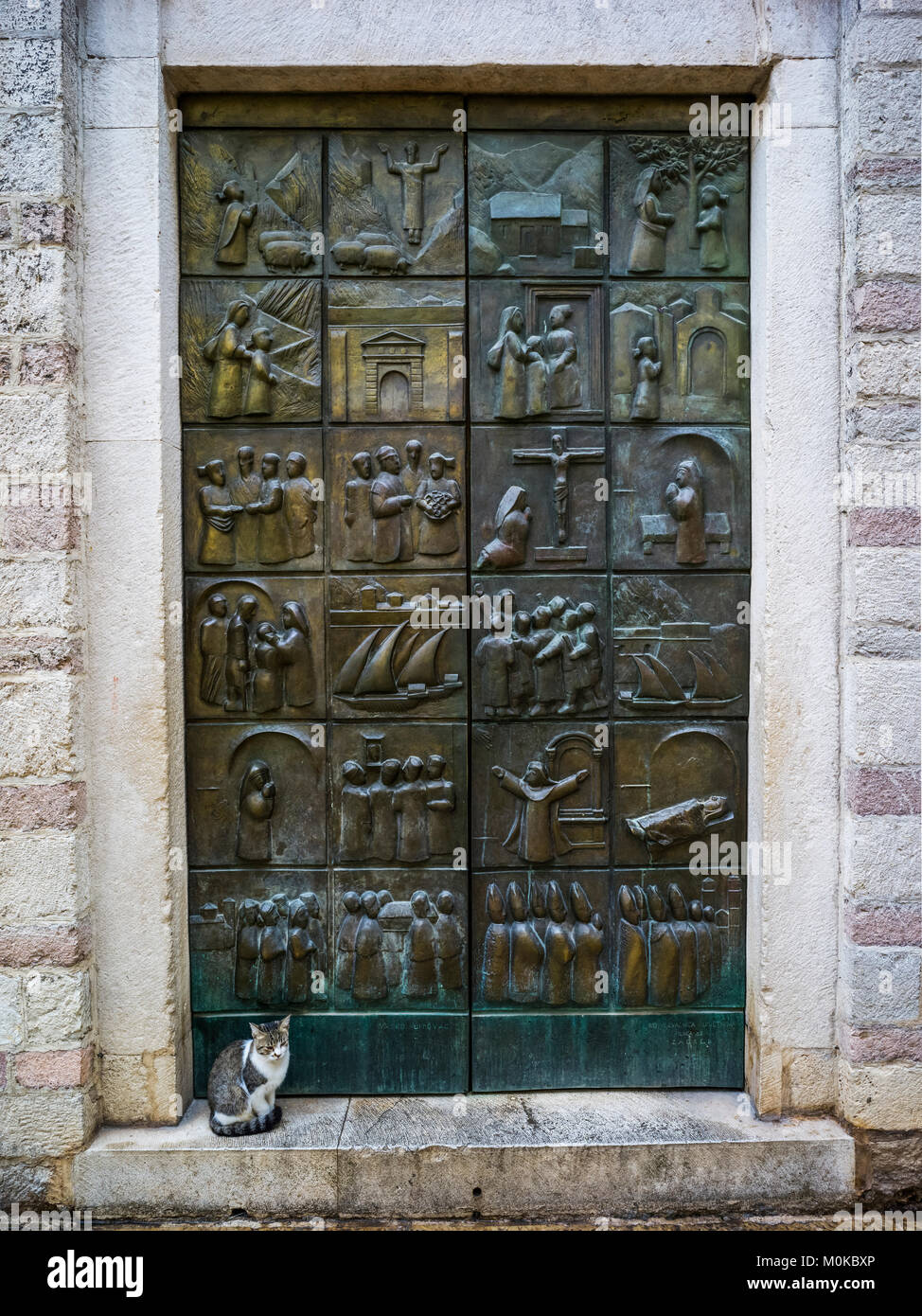 Eine Metalltür mit Piktogrammen in den Quadraten über die Oberfläche gelegt und eine Katze sitzt auf dem Step; Montenegro Stockfoto