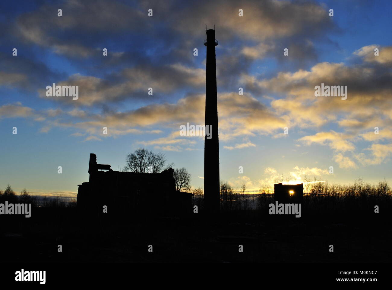 Große verlassene Fabrik mit einer hohen Pfeife im Hintergrund eines schönen Sonnenuntergangs Stockfoto