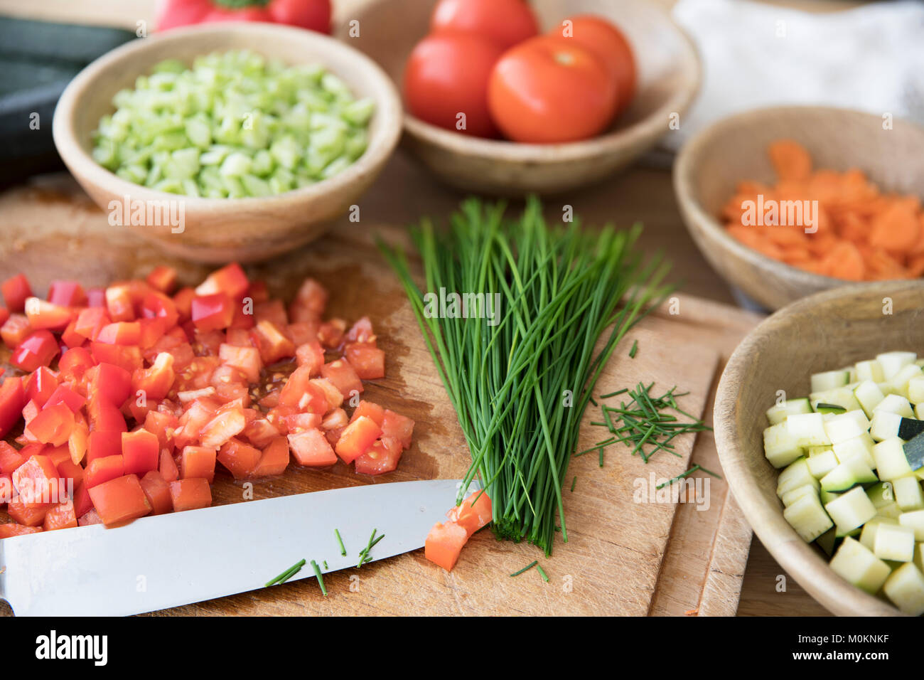 Gehackte Tomaten und Schnittlauch auf Schneidebrett mit Messer durch andere Inhaltsstoffe umgeben. Stockfoto