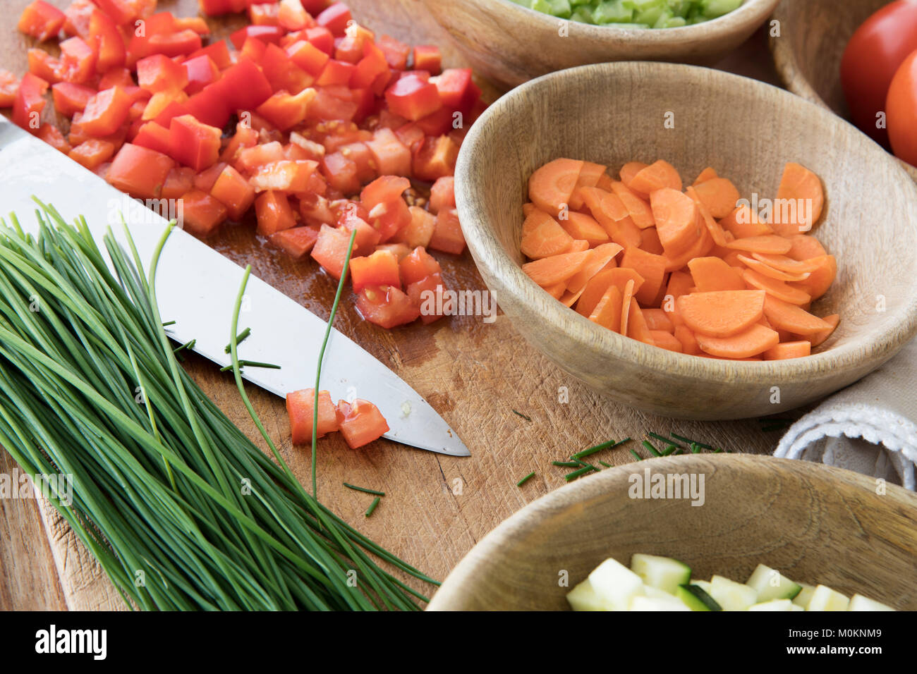 Gehackte Tomaten, Karotten, und Schnittlauch auf Schneidebrett mit Messer durch andere Inhaltsstoffe umgeben. Stockfoto