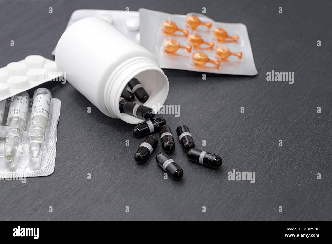 Ergänzung Kapseln sind weiße Flasche ausgegossen, Tabletten und Ampullen auf Schiefer. Medizin, Gesundheitswesen Konzept Stockfoto
