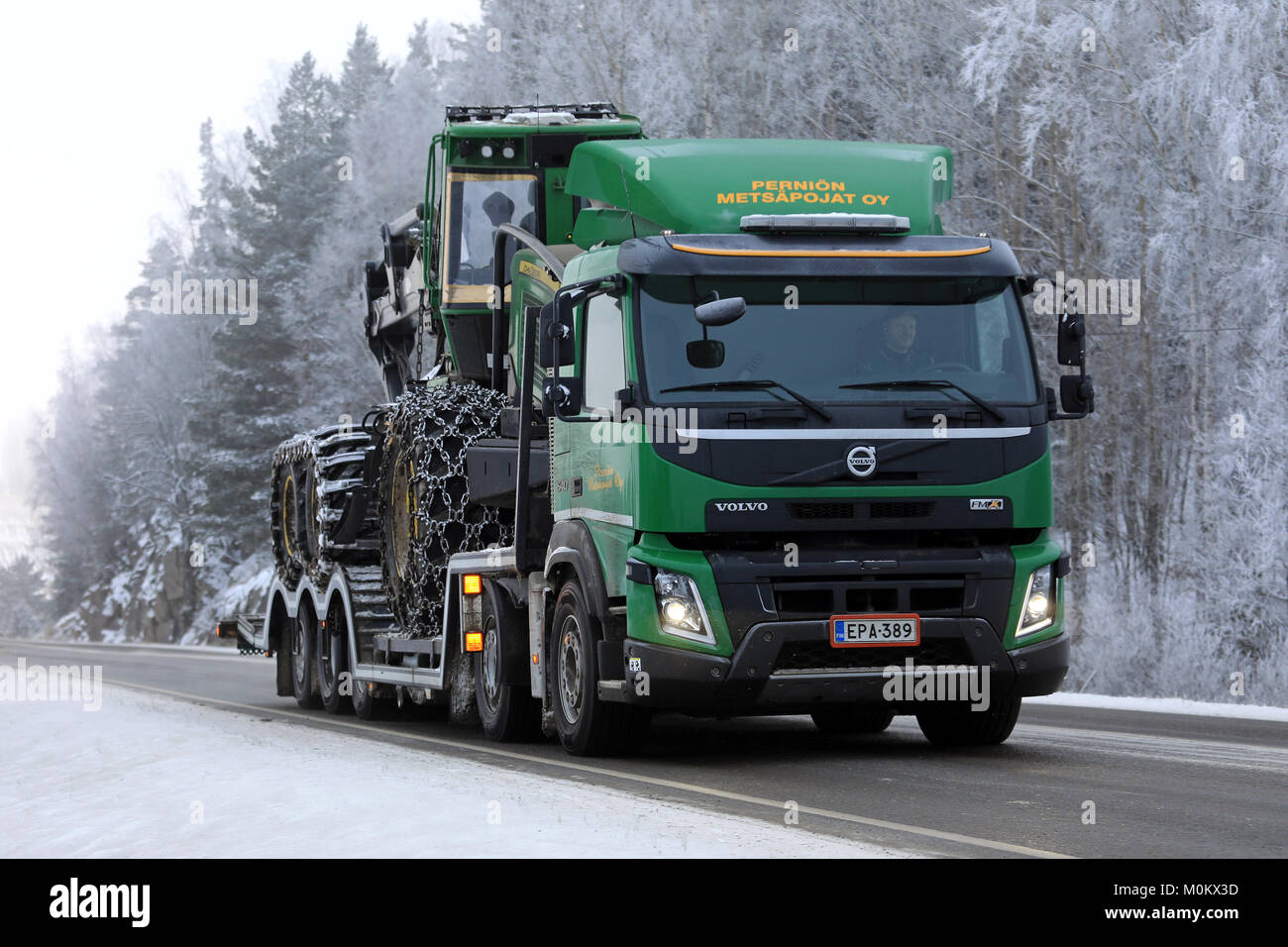 SALO, FINNLAND - Januar 20, 2018: Grün Volvo FMX Lkw hols John Deere Forstmaschinen auf Anhänger entlang der Landstraße im Winter Nebel. Stockfoto