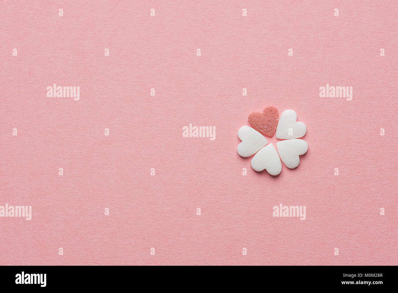 Kleine schöne Blume aus Herzform Kandiszucker weiß und rot Streusel auf Pastell rosa Hintergrund. Valentinstag Muttertag Kinder liebe Kreativität Stockfoto