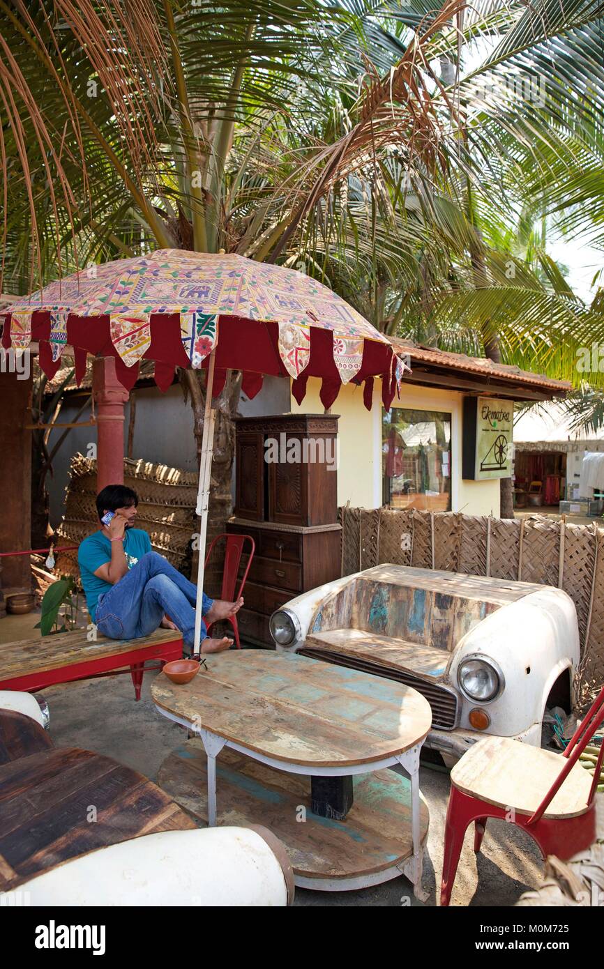 Indien, Goa Morjim Beach, Mann auf der möblierten Terrasse mit decoraion Elemente unter den Kokospalmen, in der Nähe vom Strand Stockfoto