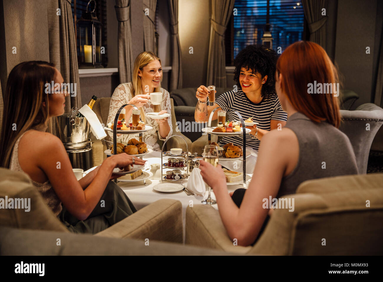 Vier Frauen sitzen den Nachmittagstee. Sie reden und Essen und Sie haben Champagner und Kaffee. Stockfoto