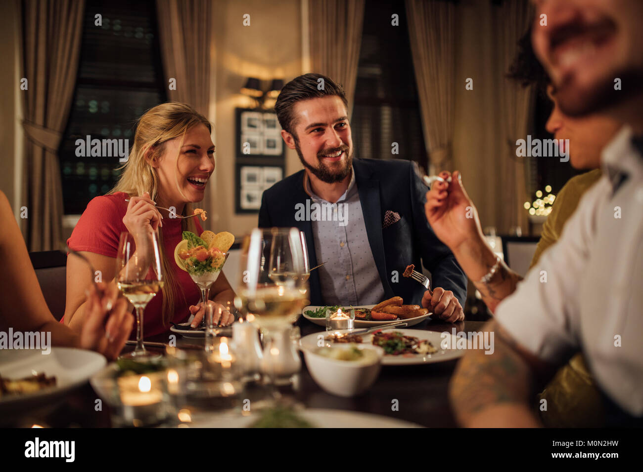 Mitte der erwachsenen Paare sind Geselligkeit über eine Mahlzeit in einem Restaurant. Sie essen und trinken Champagner beim Lachen und Reden. Stockfoto