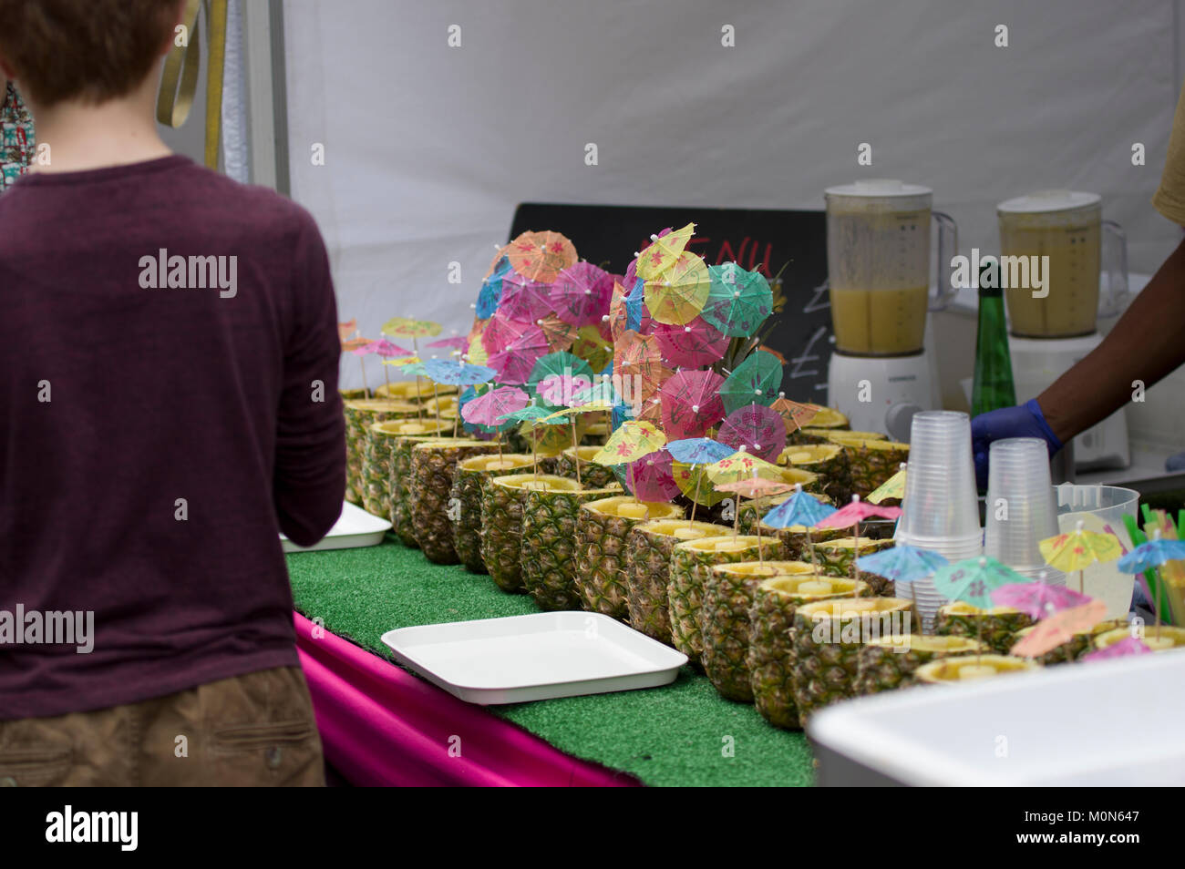 Eine Reihe von frischen Ananas und bunten Cocktail Sonnenschirme an einem Straßenfest in Marlyebone London England an einem sonnigen Tag Stockfoto