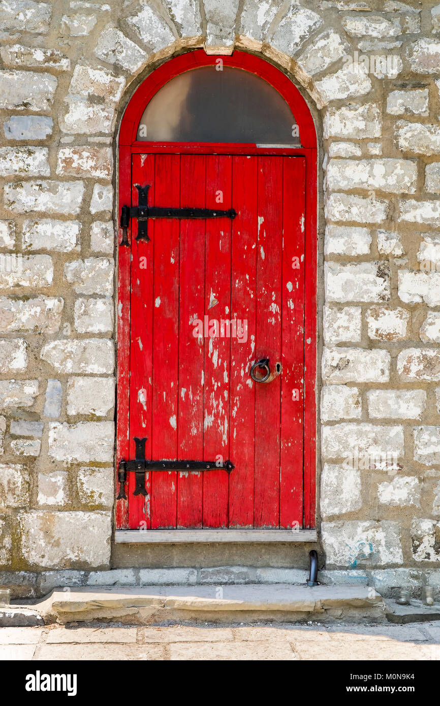 Eine alte gebogene obere rote Tür mit abblätternder Farbe und Schwarz Scharniere und Griff. Stockfoto