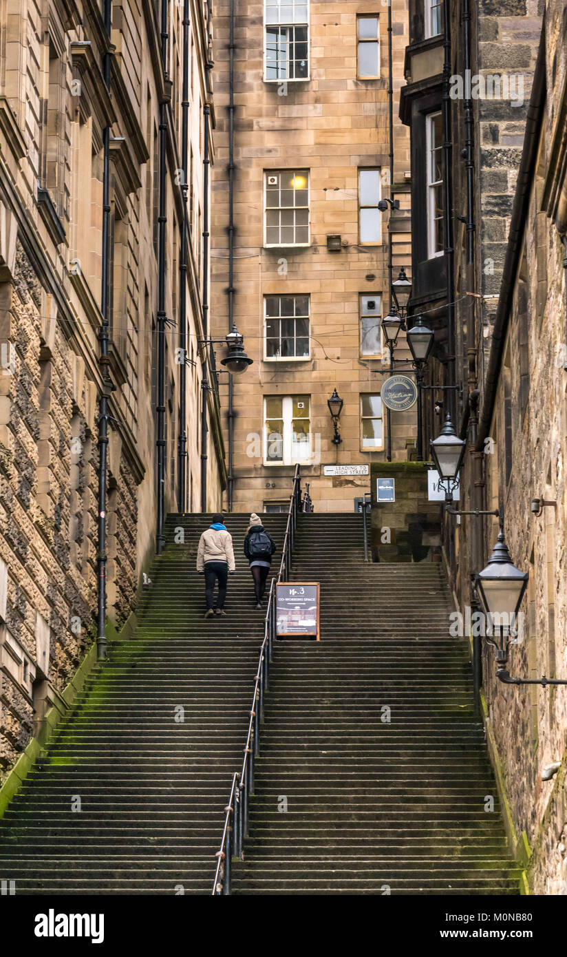 Paar klettern steile Treppe Warriston's Schließen, Cockburn Street zur Royal Mile, Edinburgh, Schottland, Großbritannien mit mietskasernen Gebäude und altmodische Lampen Stockfoto