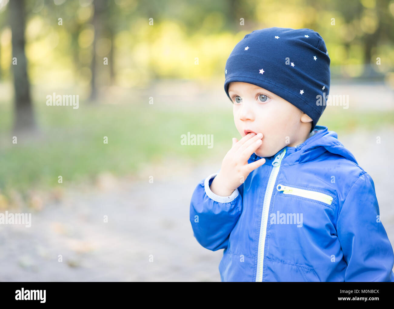 Baby Junge mit der Kappe an der Park legt seine Finger in seinen Mund mit einem Verdutzten Gesicht, erstaunt und schaut in den Weltraum. Stockfoto