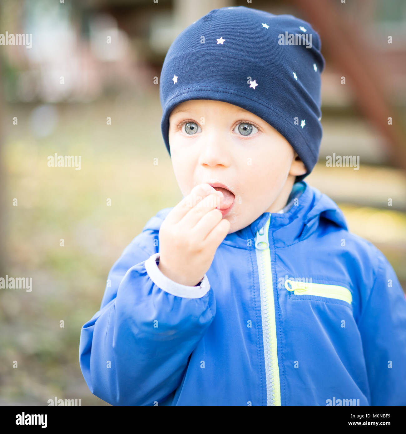 Kind Junge mit der Kappe an der Park legt seine Finger in seinen Mund mit einem Verdutzten Gesicht, erstaunt und schaut in den Weltraum. Stockfoto