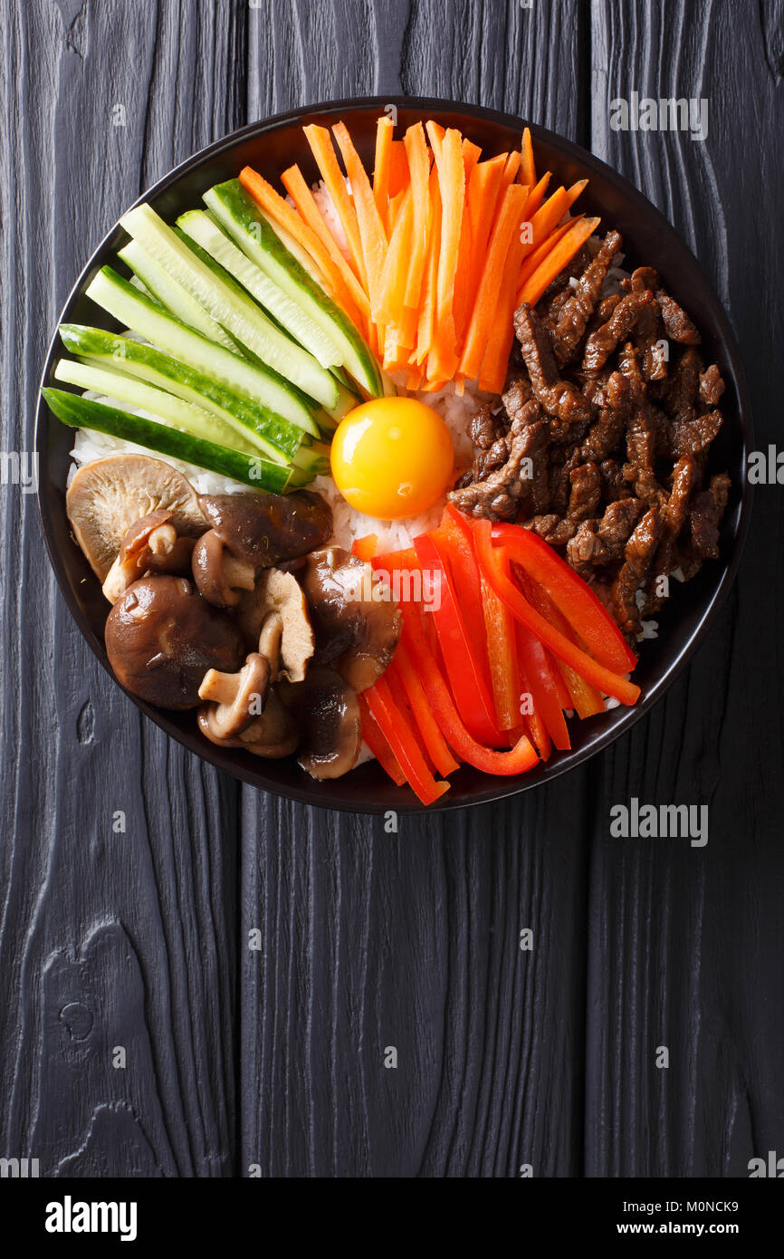 Die koreanische Küche: Bibimbap mit Rindfleisch, rohe Eigelb, Gemüse und Reis Makro auf einem Teller. Vertikal oben Ansicht von oben Stockfoto