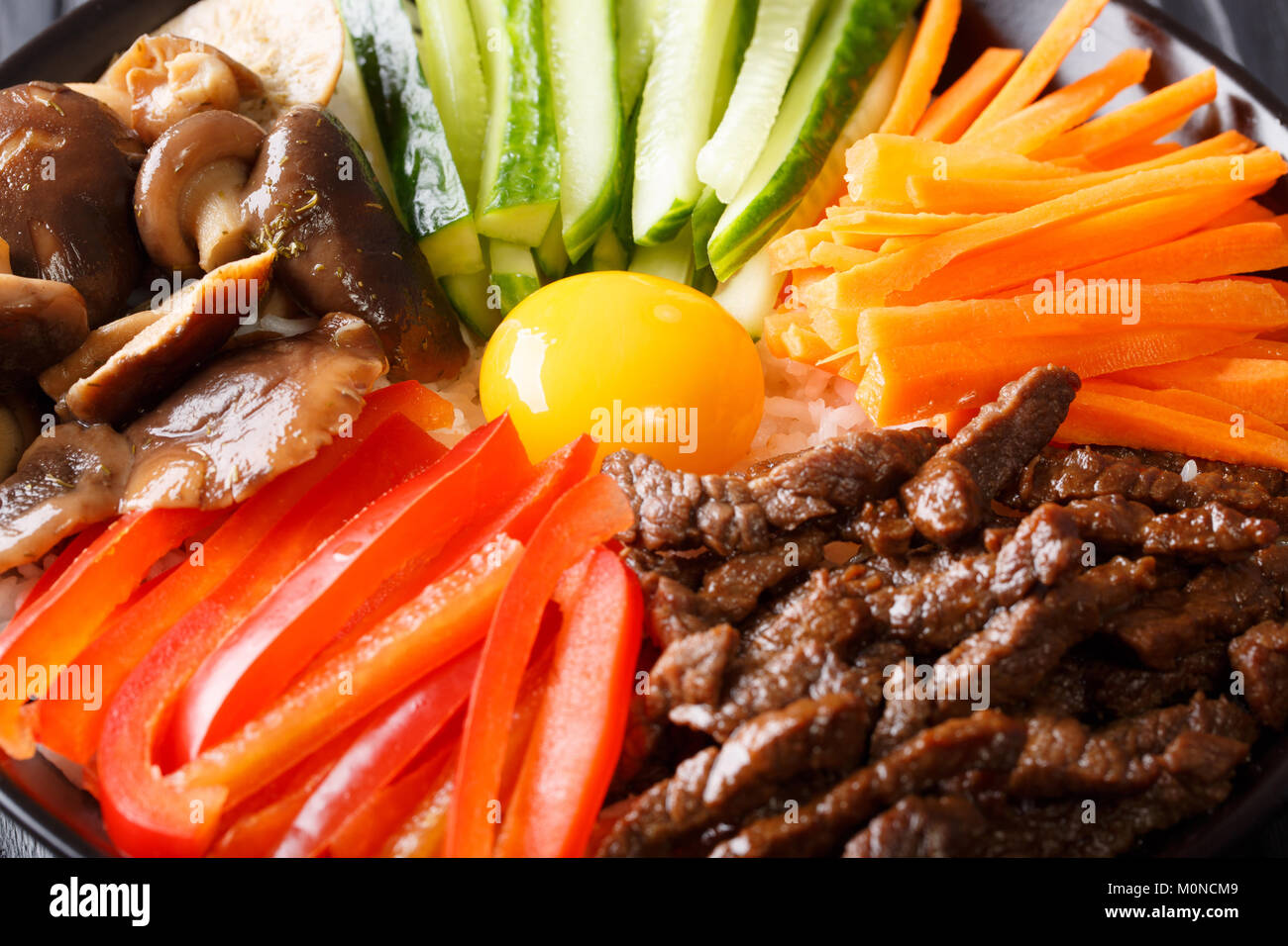 Die koreanische Küche: Bibimbap mit Rindfleisch, rohe Eigelb, Gemüse und Reis Makro auf einem Teller. Horizontale Stockfoto