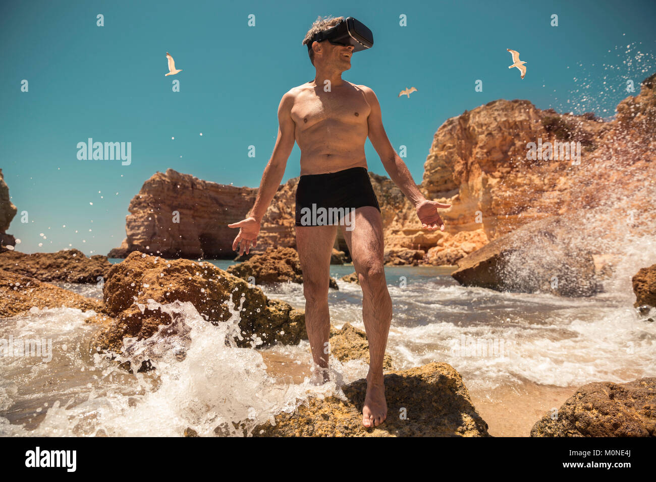 Reifen Mann mit VR-Brille zwischen Felsen am Strand Stockfoto