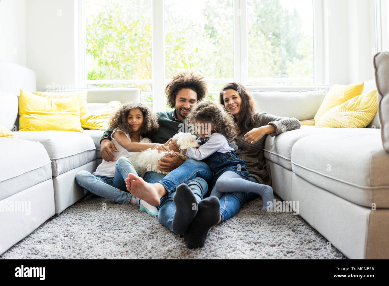 Glückliche Familie mit Hund sitzen zusammen im gemütlichen Wohnzimmer Stockfoto