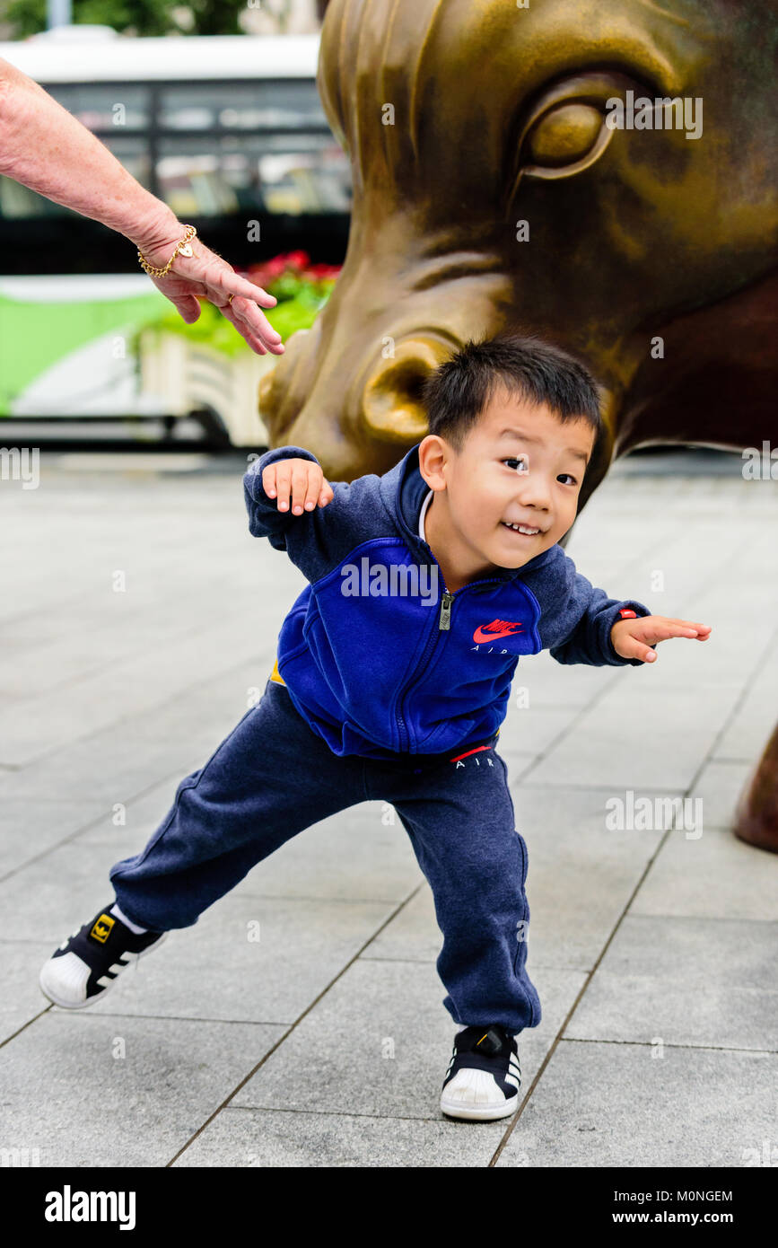 Shanghai, China. Ein junges Kind spielt und ahmt den Stier Statue im Finanzdistrikt am Bund in Shanghai, China. Credit: Benjamin Ginsberg Stockfoto