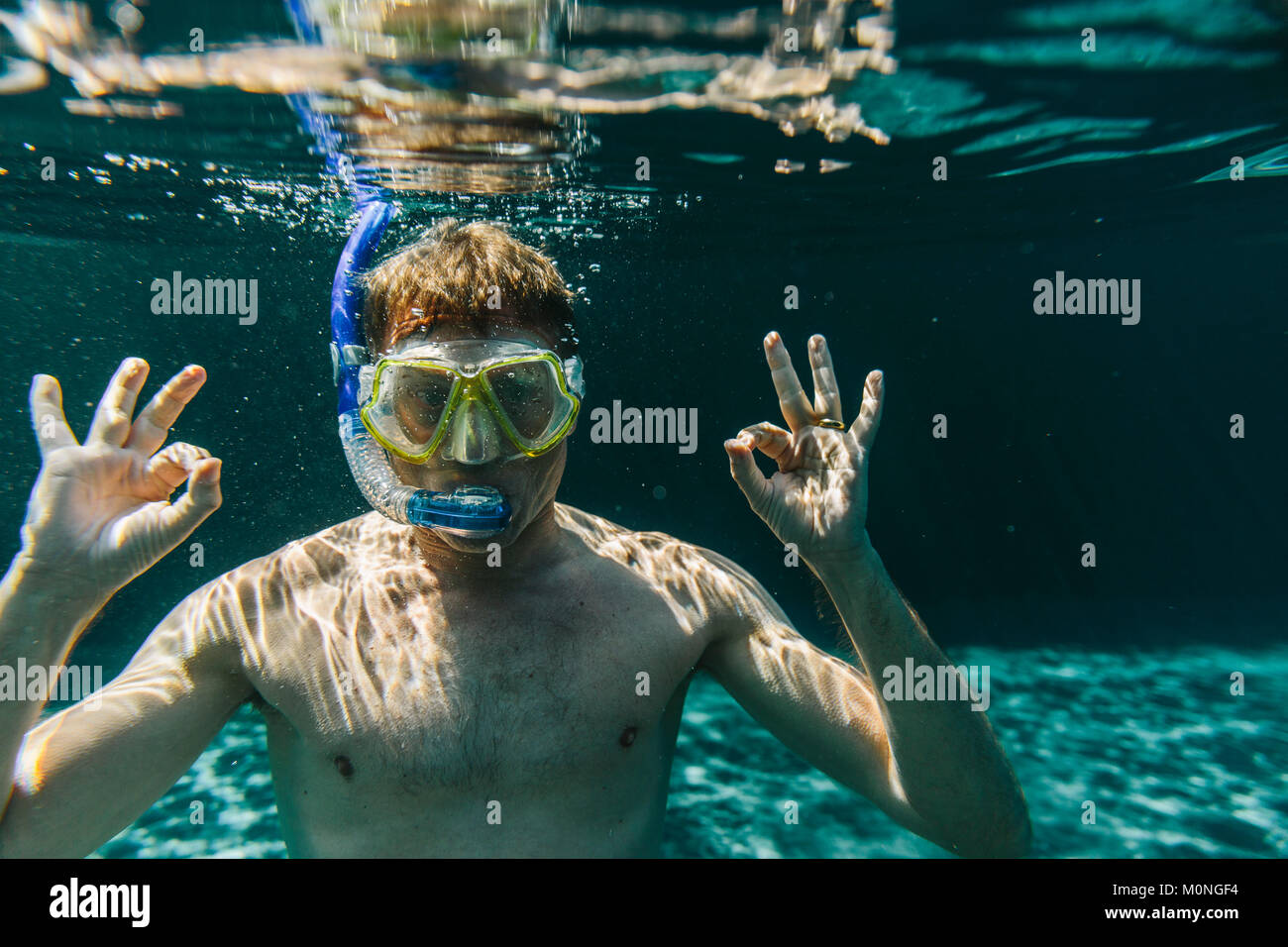 Porträt eines Mannes mit Taucherbrille und Schnorchel Unterwasser in einem Schwimmbad machen ok Zeichen Stockfoto
